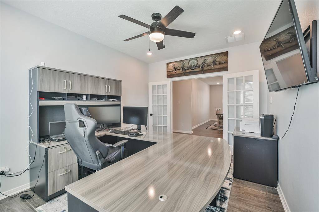 This room is a modern home office. It has a ceiling fan for ventilation and double French doors leading to another part of the house, creating an open, connected feel.