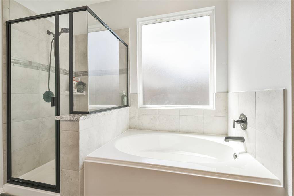 This bathroom features a modern design with a glass-enclosed shower and a separate bathtub. It has light-colored tiles and a large frosted window, creating a bright and inviting atmosphere.