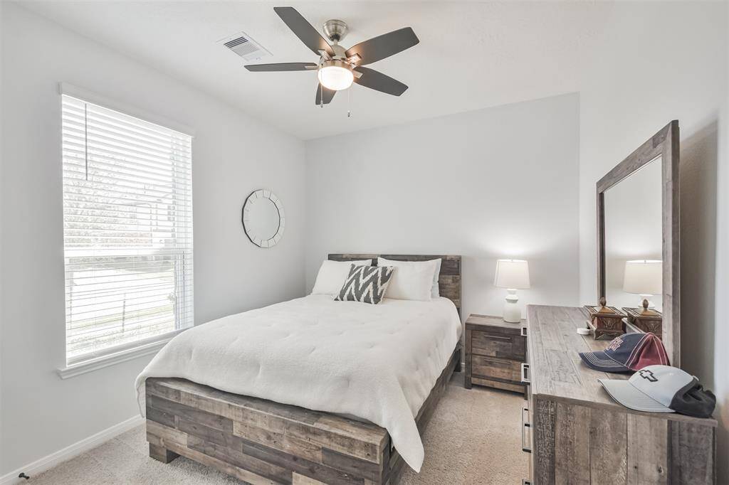This photo showcases a cozy bedroom with neutral walls, a large window allows natural light to fill the space, and a ceiling fan provides additional comfort.