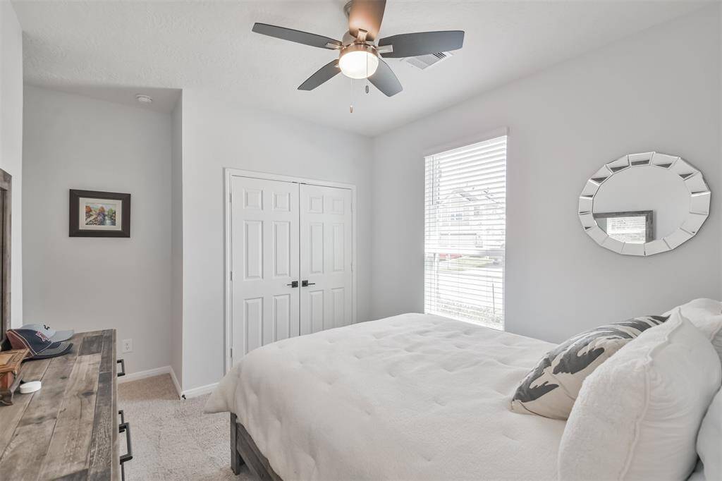 This bedroom is bright and inviting, featuring a large window with blinds, a ceiling fan, and neutral decor. It includes a bed, a dresser, and a closet with double doors, offering ample storage space.