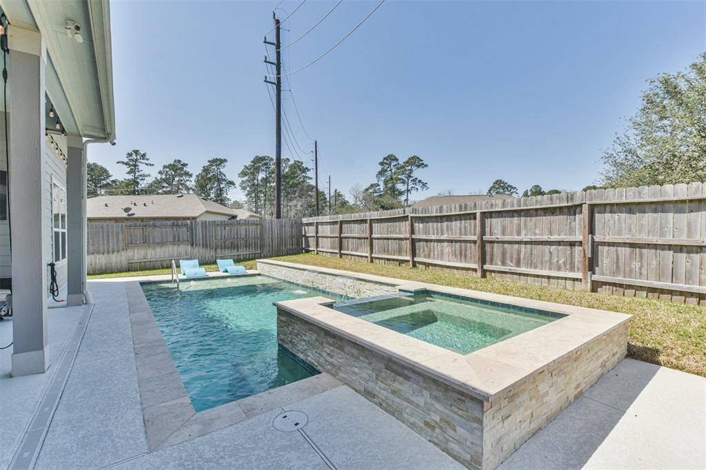 Backyard features a modern swimming pool with an attached spa, surrounded by a privacy fence. The patio offers space for relaxation and outdoor activities, ideal for enjoying sunny days.