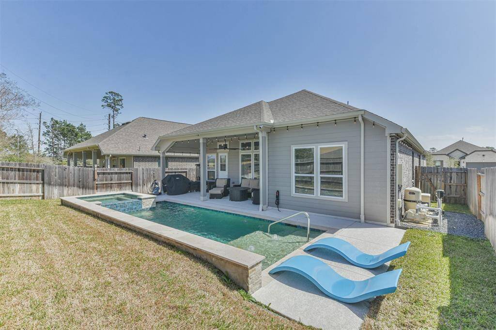 This photo shows a modern home with a covered patio and an in-ground pool in the backyard. The yard is fenced for privacy, and there are two lounge chairs beside the pool, offering a relaxing outdoor space.
