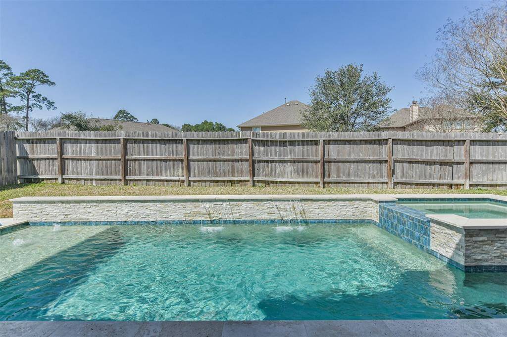 This photo showcases a backyard with a sparkling pool and spa, surrounded by a wooden privacy fence. The area is enhanced by a serene ambiance, perfect for relaxation or entertaining.