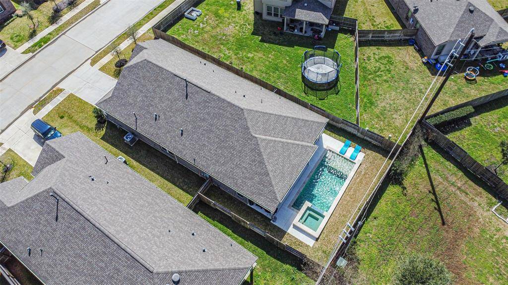 This aerial photo showcases a suburban home with a spacious backyard featuring a swimming pool and hot tub. The property is fenced, offering privacy, and is located in a neighborhood with similar homes.