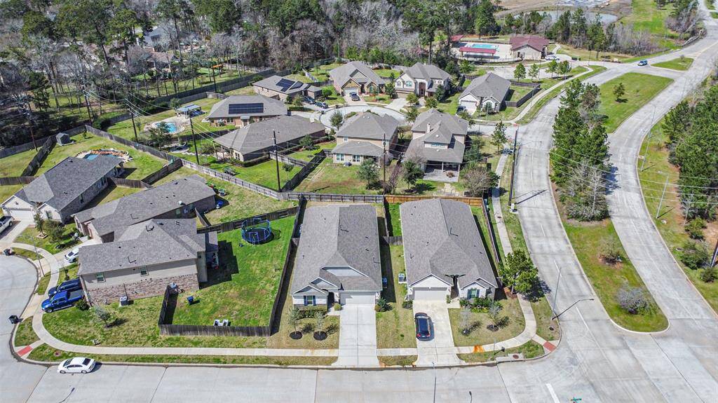 This aerial view showcases a quiet suburban neighborhood with modern single-family homes, well-maintained lawns, and fenced backyards. The area is surrounded by trees, offering a peaceful setting with curving roads and ample space between houses.