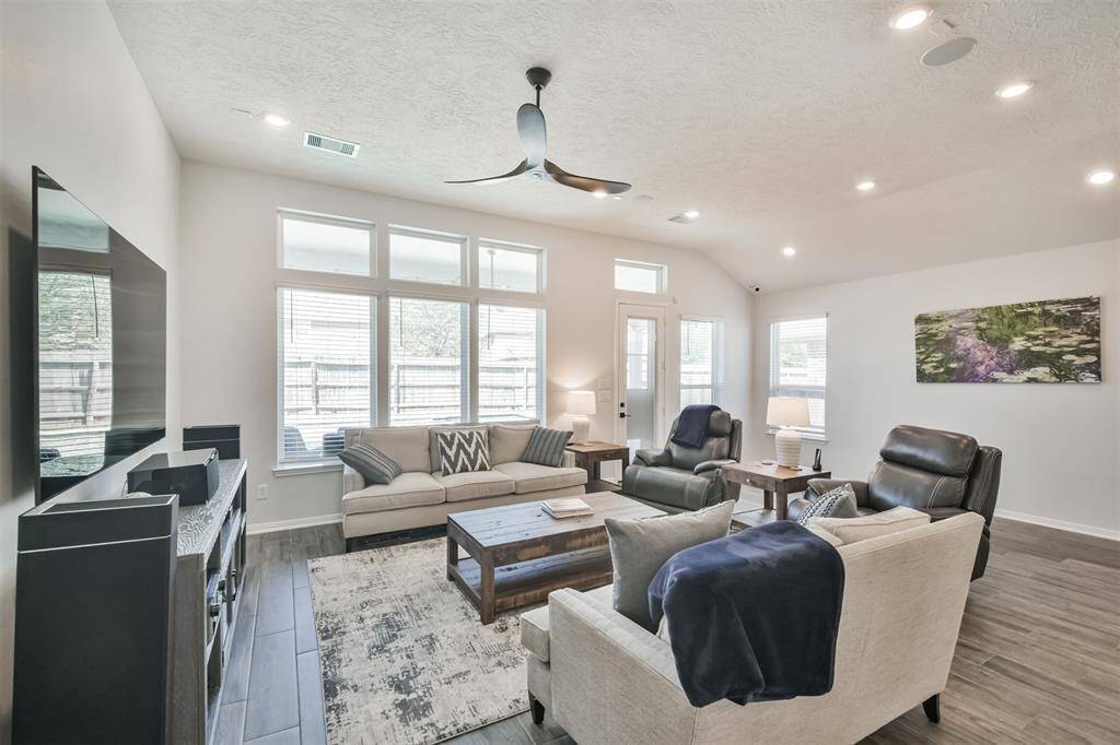 This spacious living room features large windows for ample natural light, a ceiling fan, and modern recessed lighting.