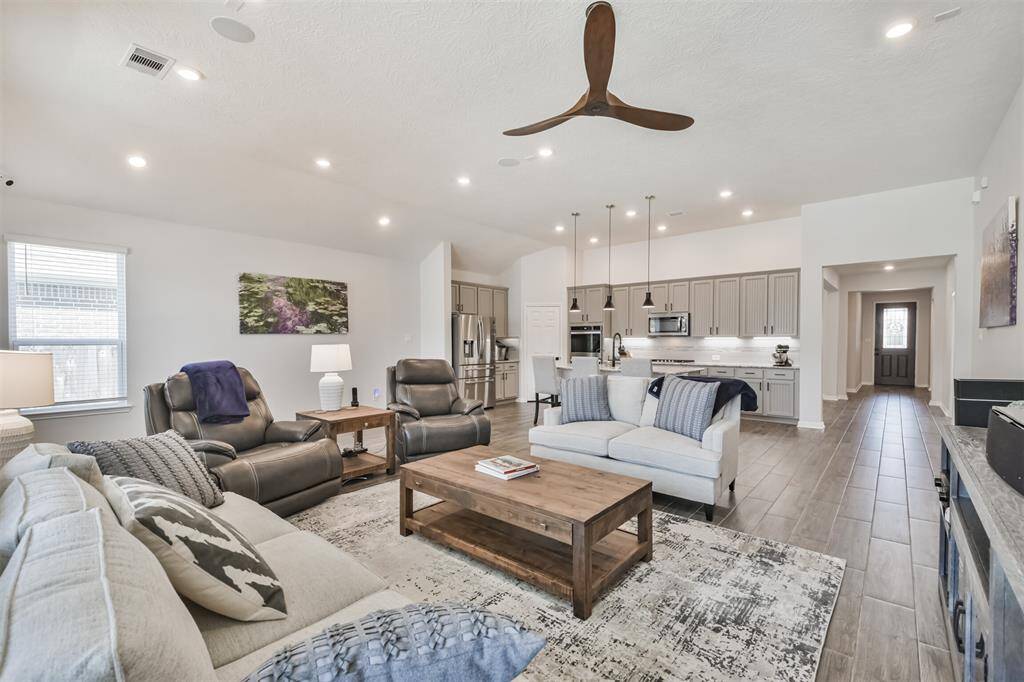 This spacious open-concept living area features a modern kitchen with stainless steel appliances and pendant lighting. The room is bright with natural light, high ceilings, and elegant tile flooring.