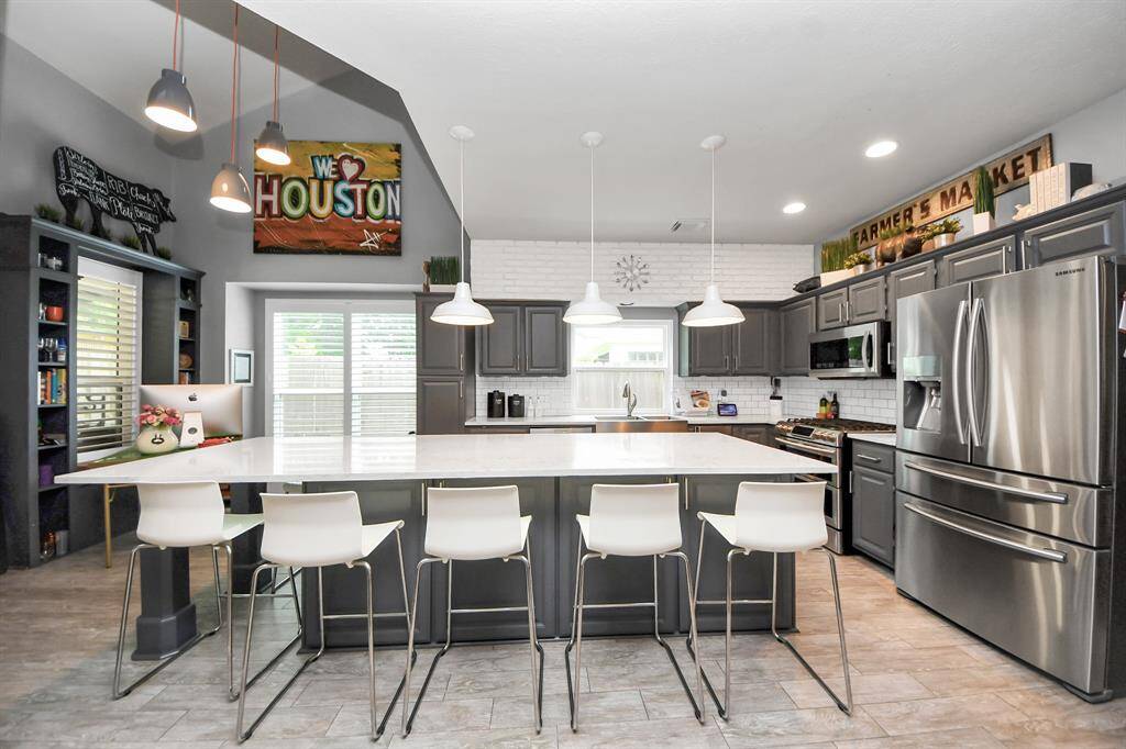 kitchen features a massive quartz island with seating for six, custom gray cabinetry, and stainless steel appliances.