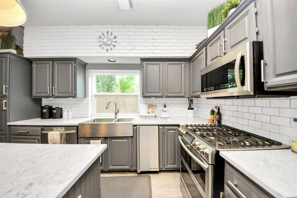 A bright and airy layout with stainless farmhouse sink, subway tile backsplash, and elegant white quartz countertops. The large window over the sink brings in natural light, creating a warm and inviting atmosphere.