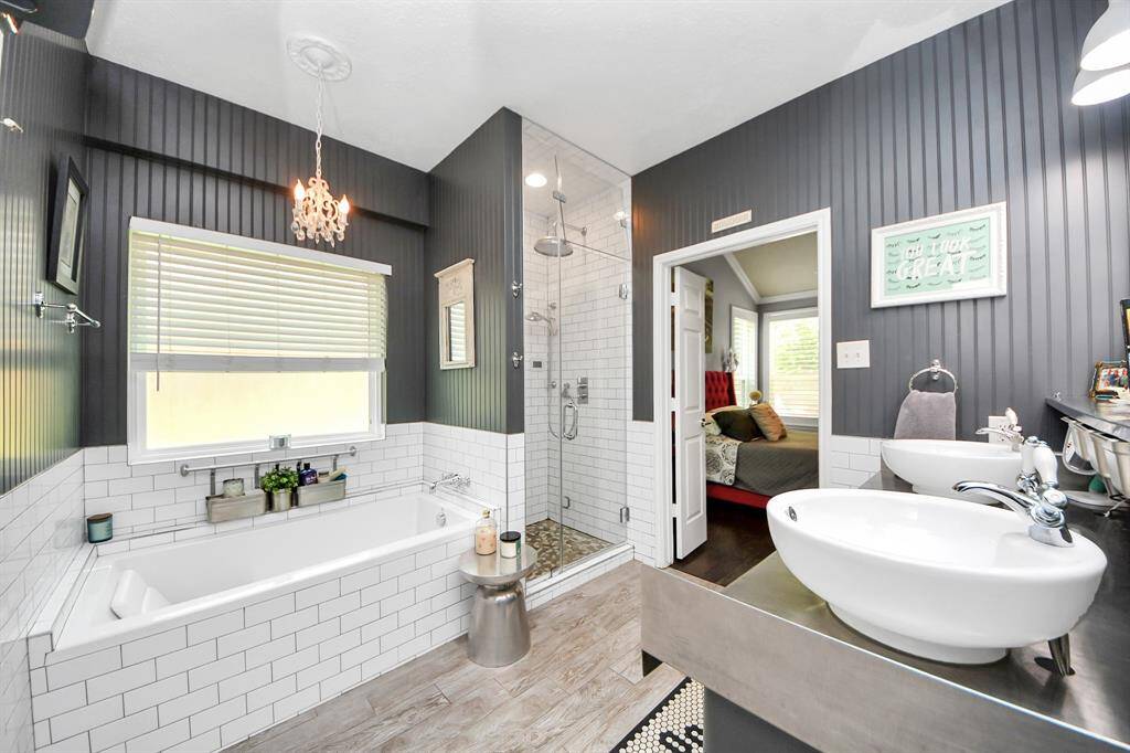 The primary bathroom features dual vanities, a soaking tub, and a walk-in shower. Dark shiplap-style paneling contrasts beautifully with the white tile and vessel sinks. A stunning chandelier adds a touch of elegance.