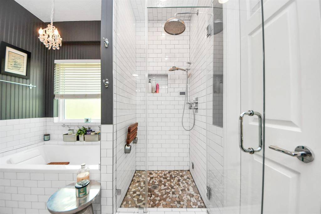 Enjoy a spa-like experience in this oversized walk-in shower with frameless glass, subway tile surround, rainfall showerhead, built-in bench, and pebble stone flooring. The perfect combination of function and indulgence.