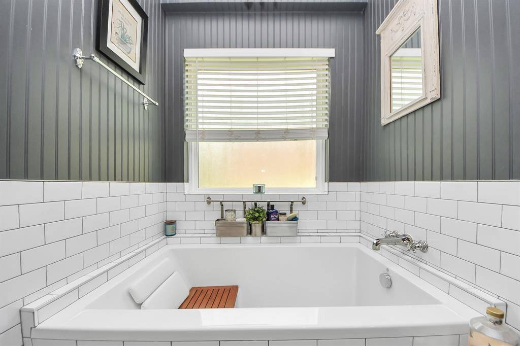 Unwind in the deep soaking tub accented by white subway tile, wall paneling, and a tranquil window with privacy glass. Thoughtful storage nooks and classic chrome fixtures complete the serene setting.
