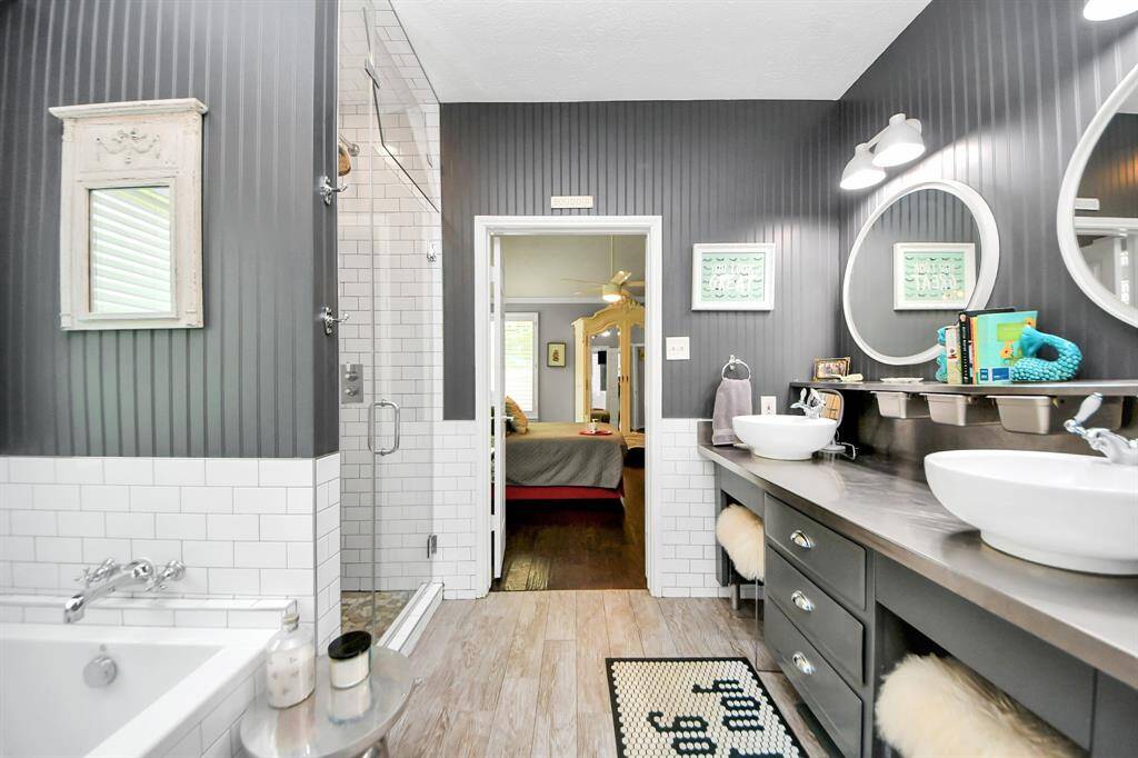 A modern dual vanity with vessel sinks and round mirrors provides ample space and storage. Subway tile, wood-look floors, and rich wall tones create a clean yet cozy vibe for your daily routine.