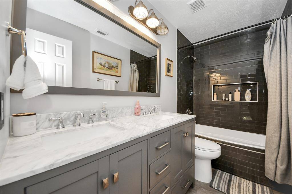 The secondary bath features sleek dark subway tile in the shower-tub combo, a Quartz countertop with dual sinks, and updated fixtures throughout. A chic blend of modern style and functionality.