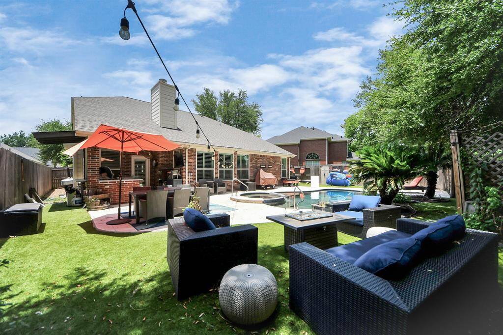 This entertainer’s backyard features multiple seating zones and an inviting pool and spa. String lights, lush greenery, and artificial turf create a resort-style vibe perfect for relaxing or hosting.
