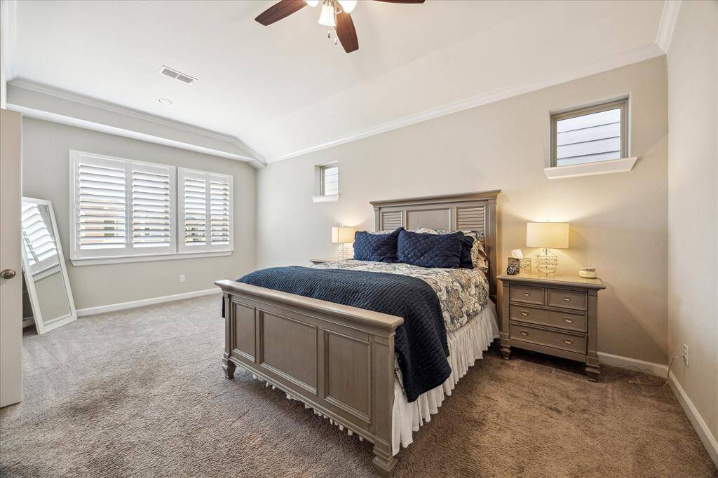 Unwind in this serene primary retreat featuring tray ceilings, soft natural light, and elegant plantation shutters for added privacy and style.