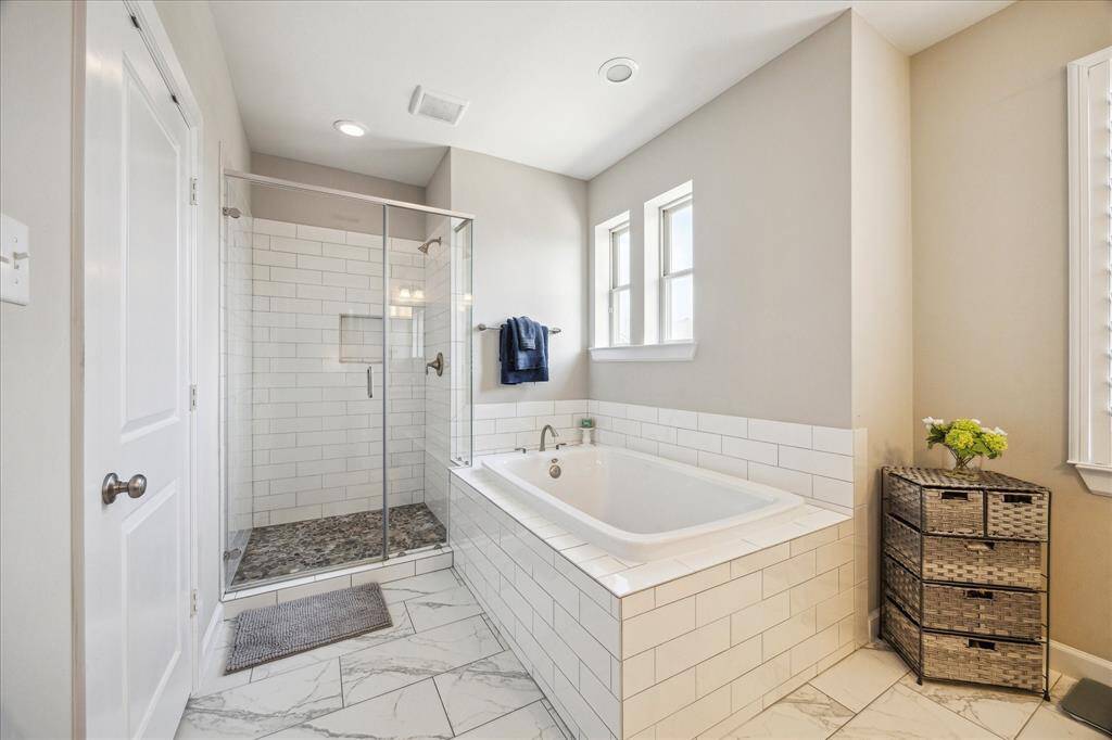 Indulge in spa-like comfort with a soaking tub, frameless glass shower, and elegant tile details in this serene primary bathroom retreat.