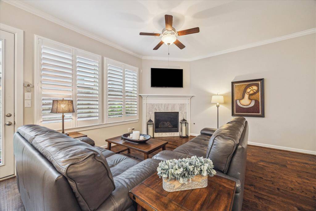 Cozy up by the elegant gas fireplace in this inviting living area, complete with plantation shutters, warm wood floors, and abundant natural light.