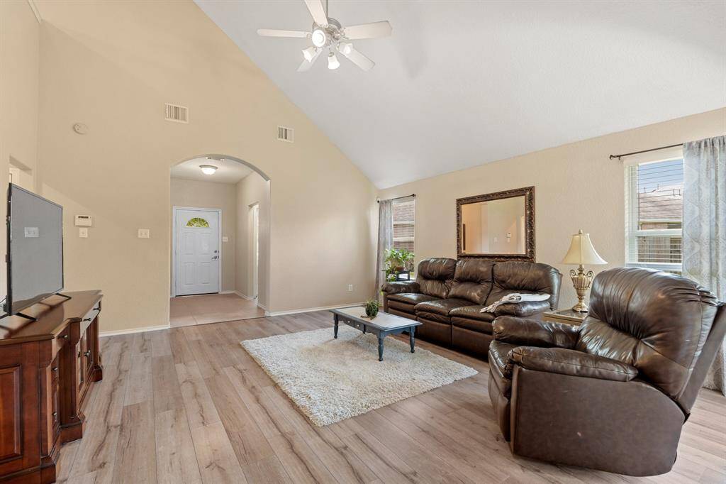 Bright and spacious living room with high ceilings and a ceiling fan with wood-styled flooring.