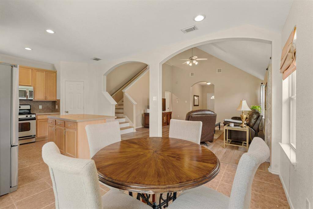 This open-concept living area features a dining space, a modern kitchen with stainless steel appliances, and a spacious living room with vaulted ceilings and abundant natural light.