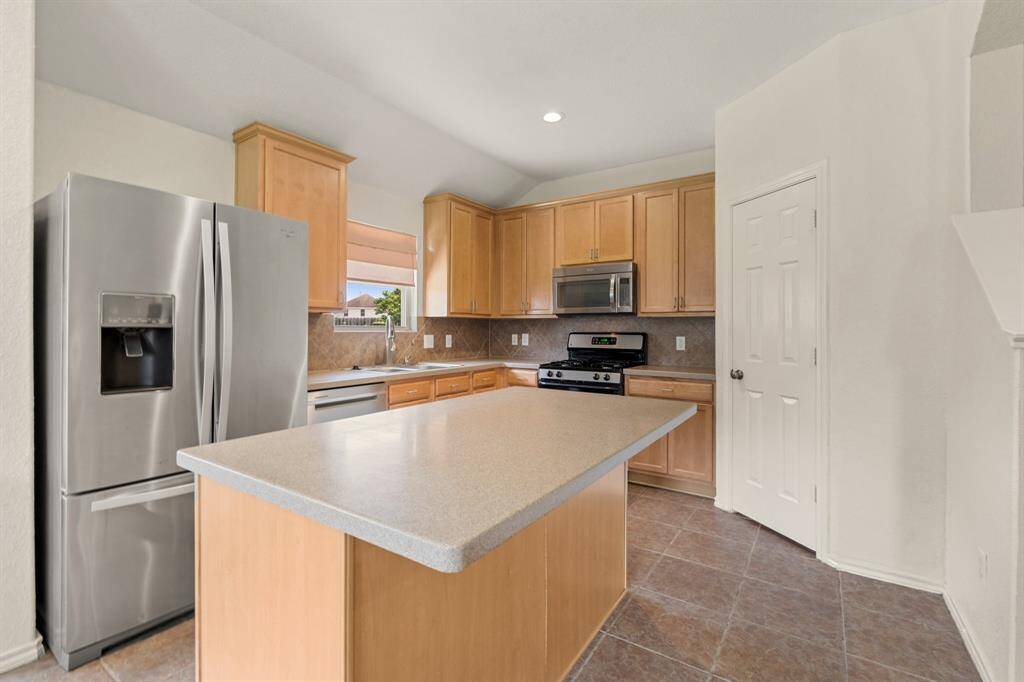 Modern stainless steel appliances, light wood cabinets, and a spacious island with a sleek countertop.