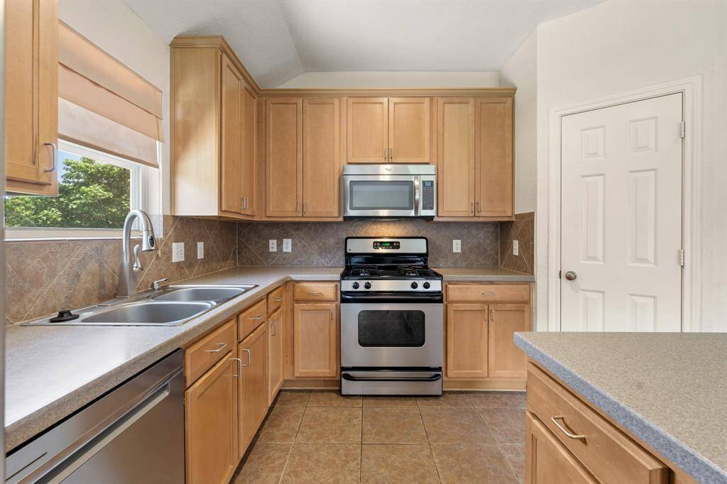 This kitchen has a double sink, tile flooring, and ample natural light from a window above the sink. The layout is functional and modern, ideal for cooking and entertaining.