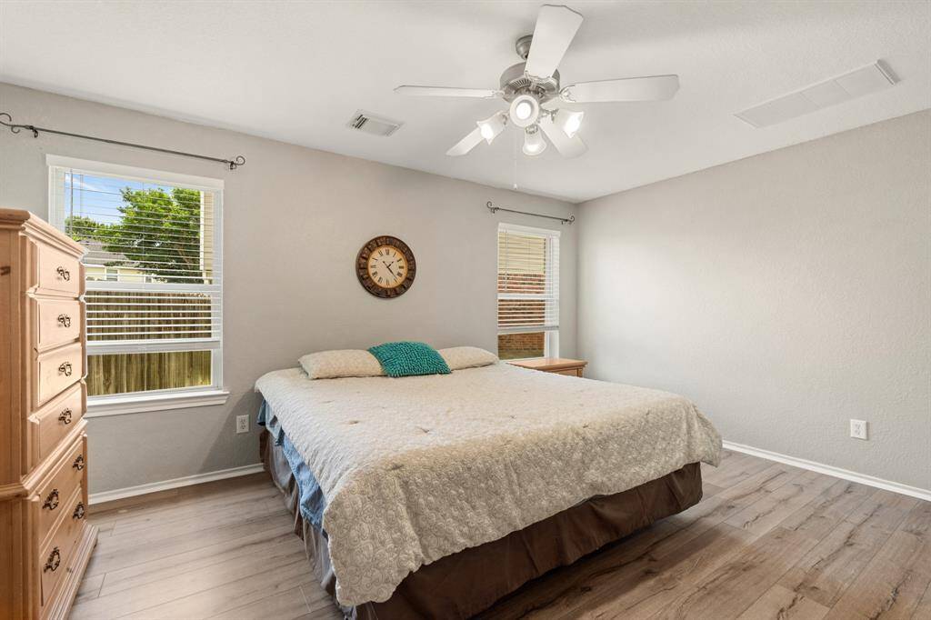 Primary bedroom downstairs with neutral walls and wood-styled flooring, featuring a ceiling fan and ample natural light from two windows.