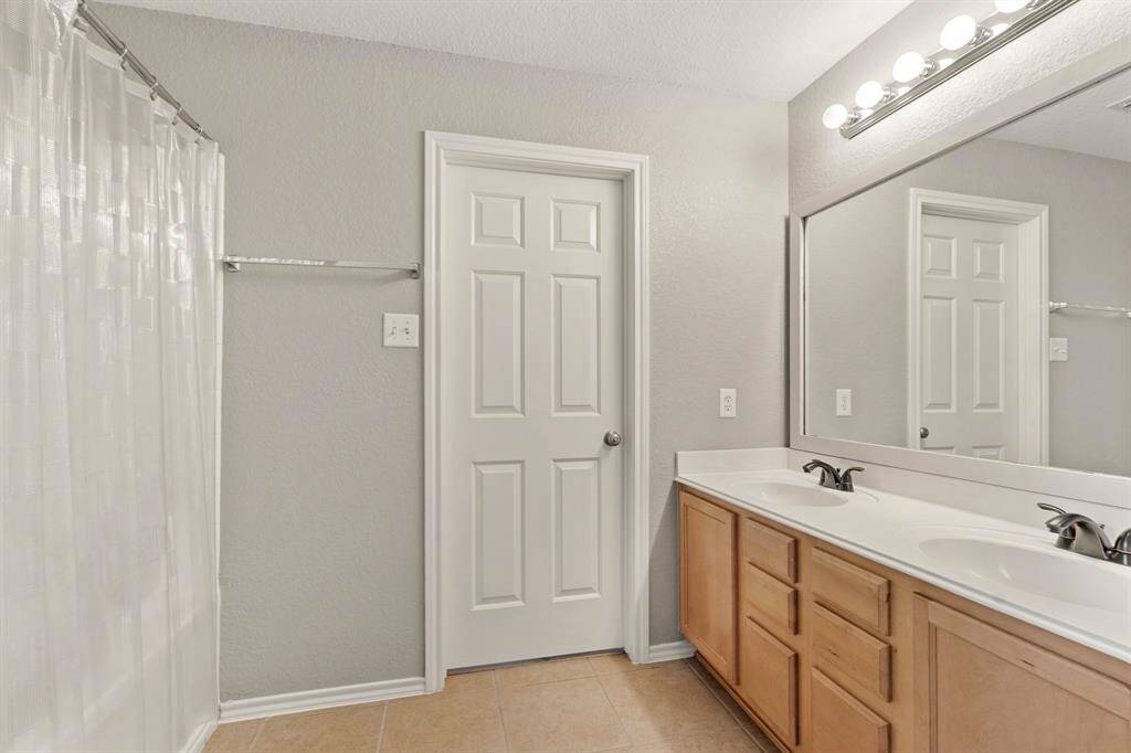 Primary bath features a clean, modern design with a white vanity and sink, a large mirror with a wooden frame, and a combined bathtub and shower.