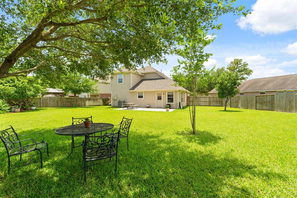 Lush green grass, a few trees providing shade, and a patio area perfect for relaxing or entertaining.