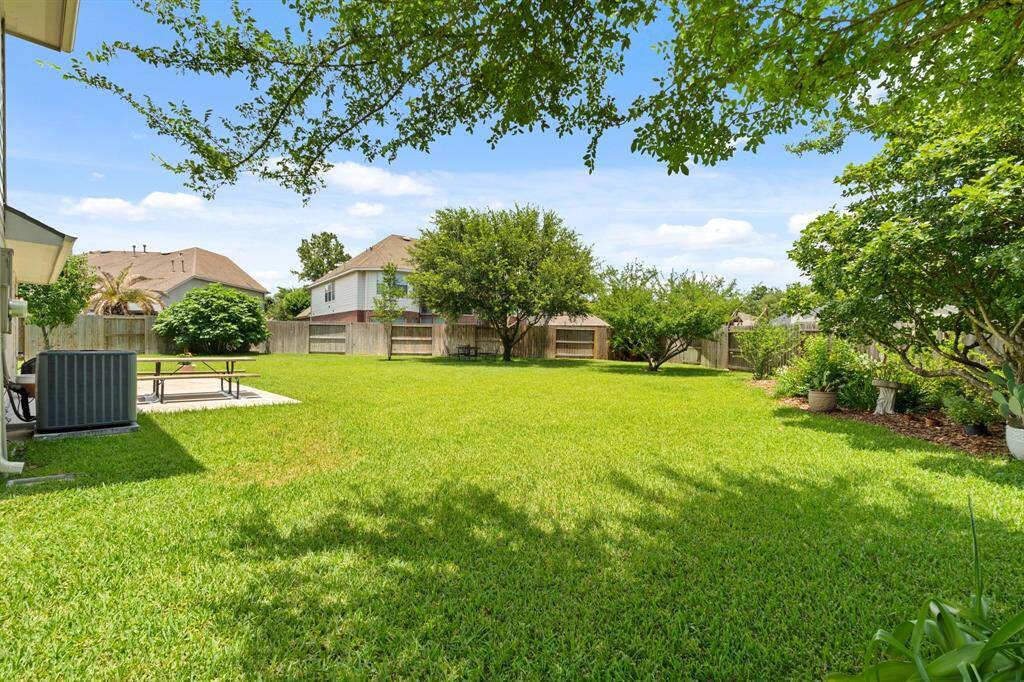 Spacious backyard with lush green grass, mature trees, and a fenced perimeter, offering privacy and ample space for outdoor activities.