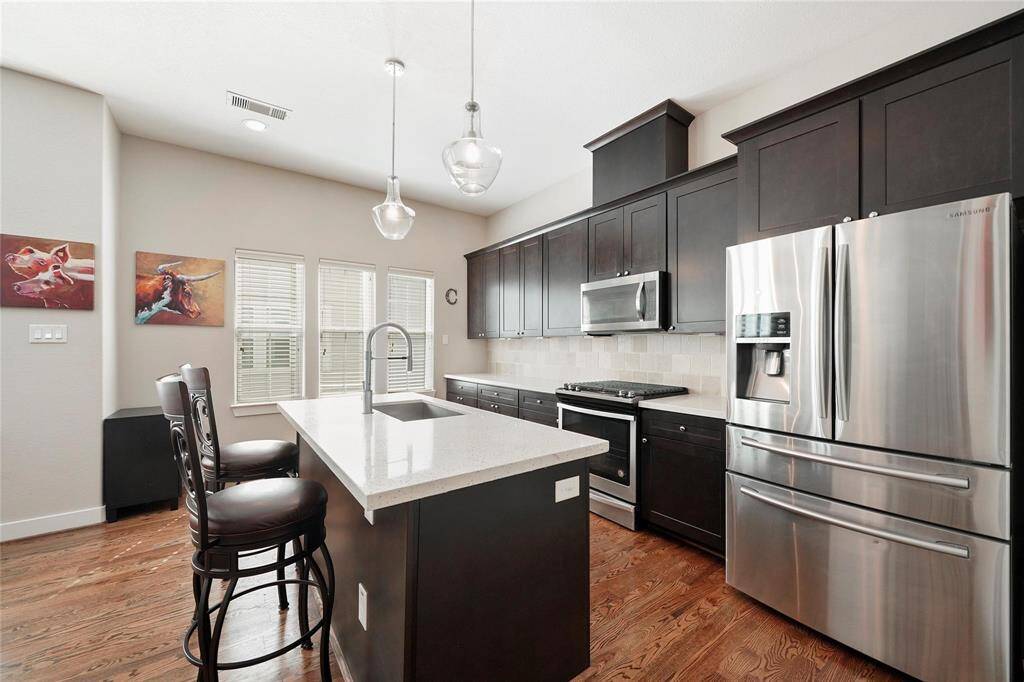 Island kitchen with stainless steel appliances including the refrigerator.  Hardwood floors.  The three windows allow a lot of light in.