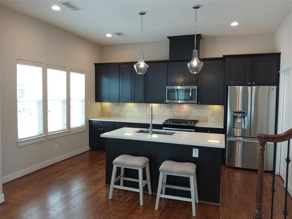 Island kitchen with stained wood cabinets, stainless steel appliances including the refrigerator.  Three windows let the light fill the room.