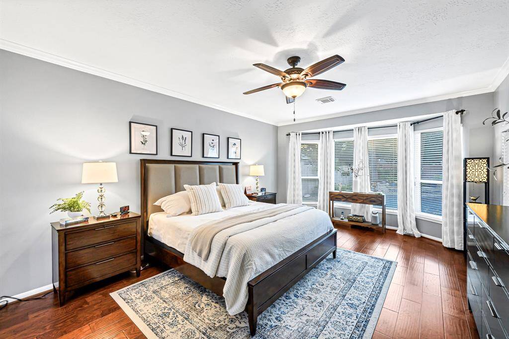 A SERENE AND INVITING PRIMARY BEDROOM SUITE WITH HARDWOOD FLOORS, LARGE BAY WINDOWS LOOKING OUT TO A WELL LANDSCAPED BACKYARD