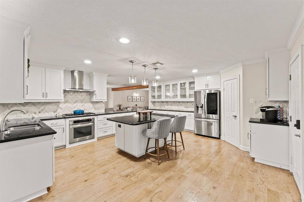 Kitchen island charging station, gas cooktop, with stainless vent-hood as well as a combination of glass and privacy kitchen cabinets.