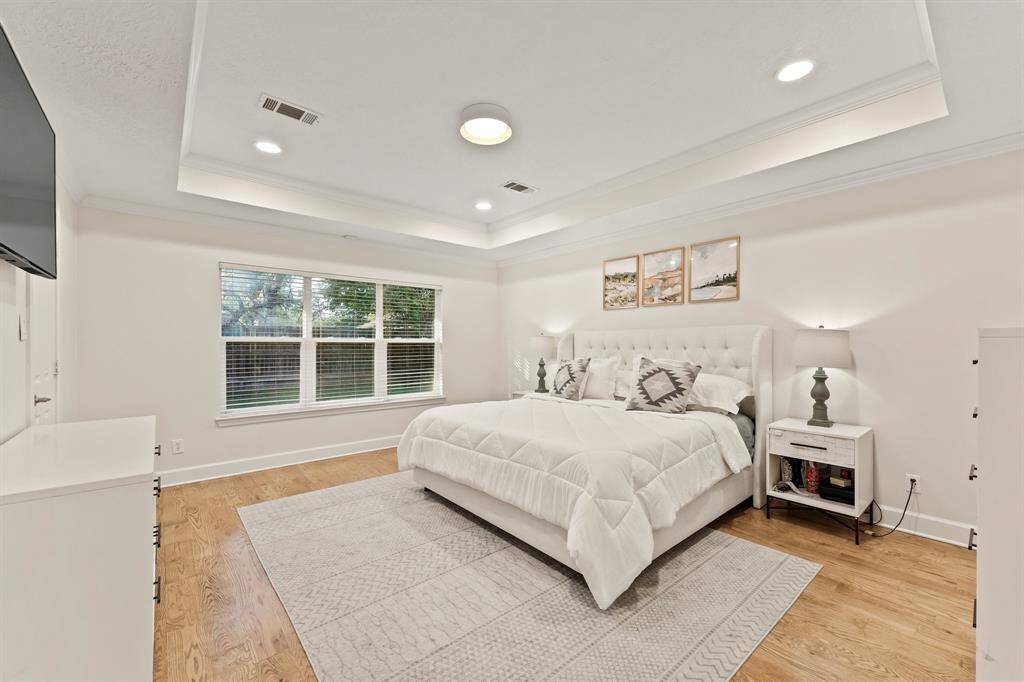 Primary bedroom with trey ceilings, recessed lighting, hardwood floors, crown molding and windows facing north.