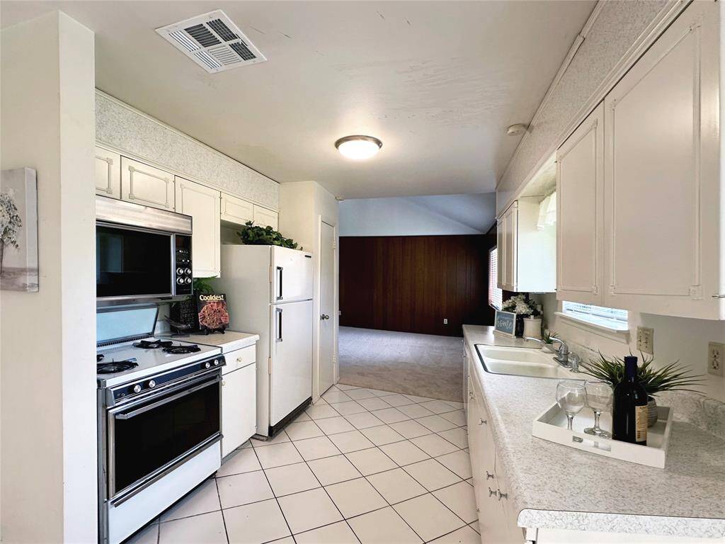 Bright kitchen with white cabinetry, tiled flooring, and appliances. Ample counter space and natural light create a welcoming atmosphere. Adjacent to the freshly carpeted living area.