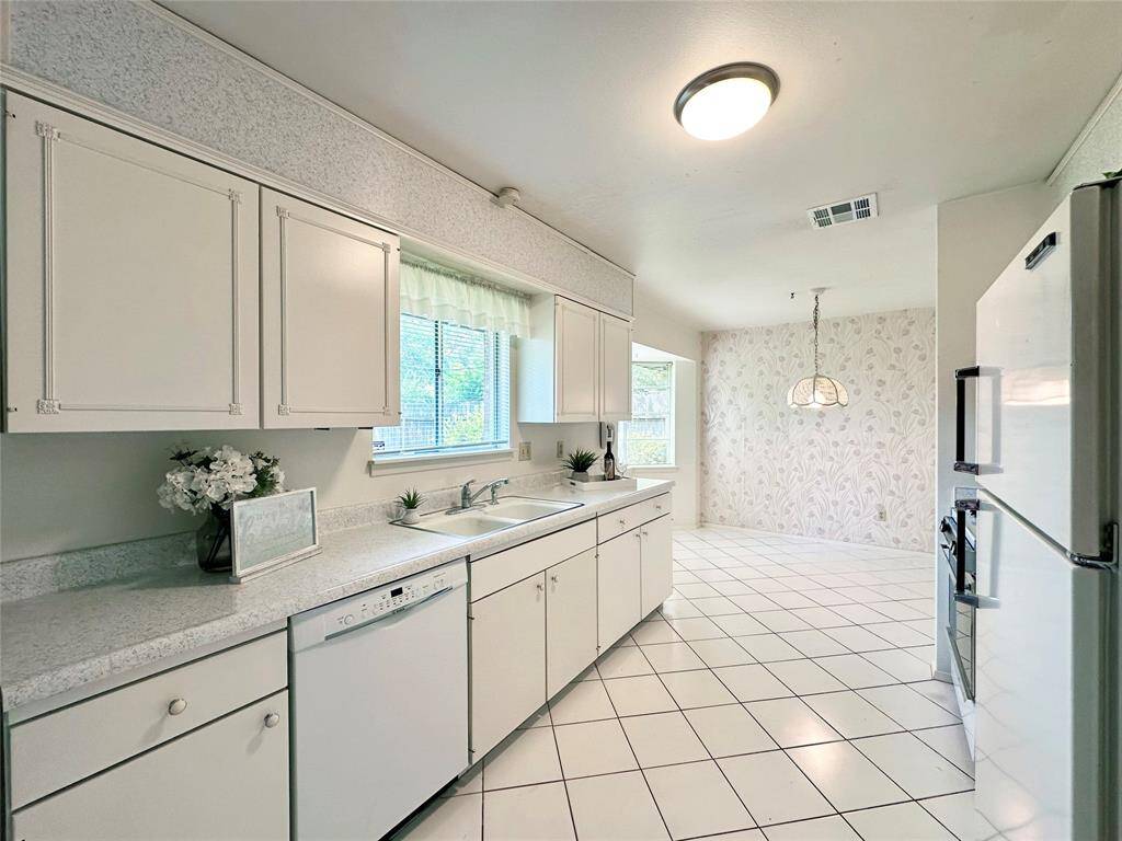 Bright, spacious kitchen with white cabinetry, tiled flooring, and appliances. Features a cozy breakfast nook with large windows and a decorative light fixture, offering a pleasant view and ample natural light.