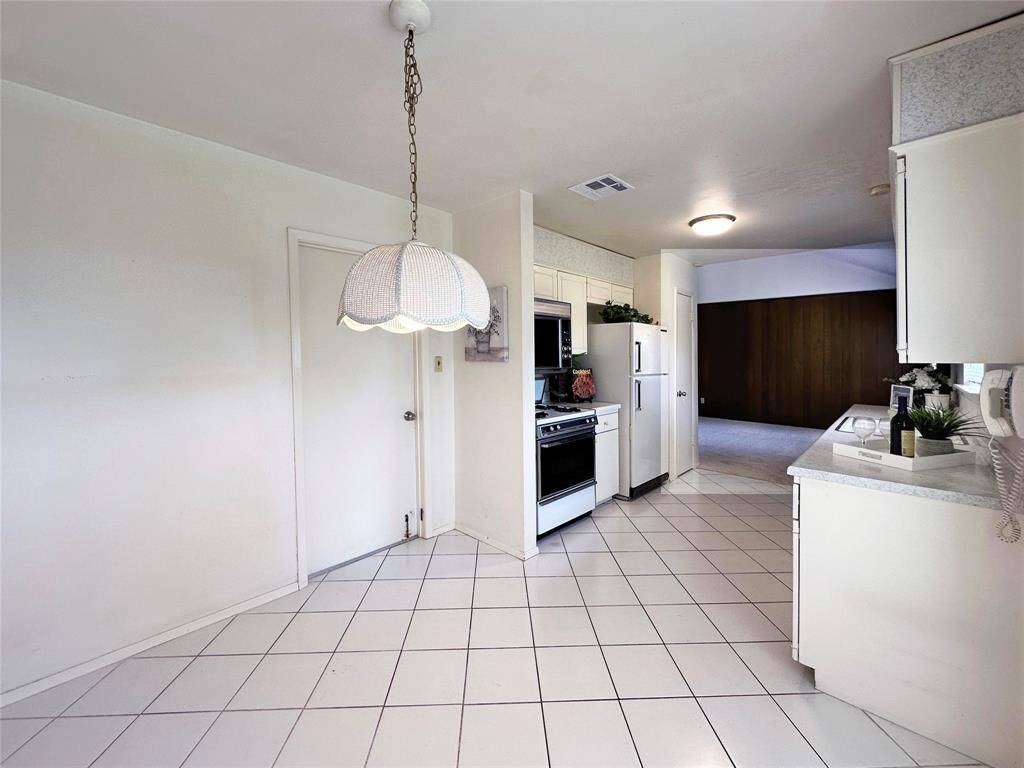 Bright kitchen with white tile flooring, and ample counter space. Includes white appliances and cabinetry, with an open view to the living area.