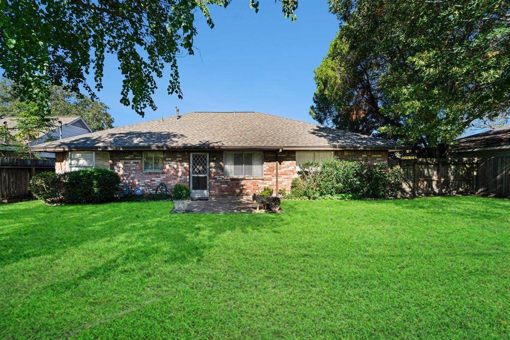 This photo showcases a charming brick house with a spacious backyard. It features a central back door, surrounded by lush greenery and trees, offering a serene and private outdoor space.