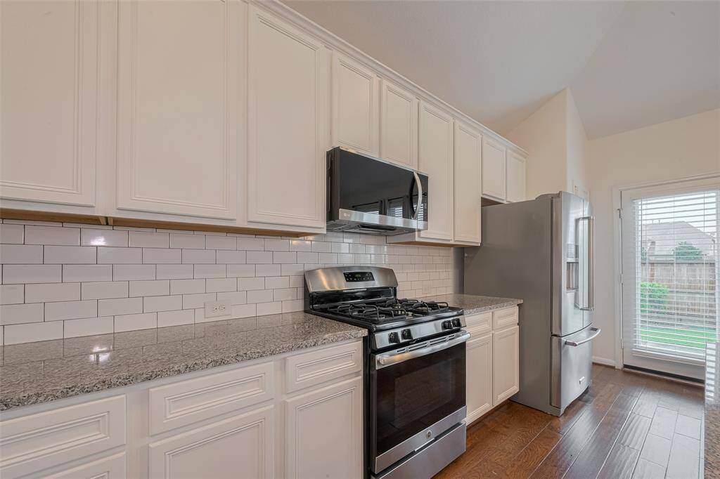 Kitchen is enhanced by a classic subway tile backsplash, adding a clean and timeless touch to the kitchen design. Distressed hardwood floors continue throughout, offering warmth and character. A convenient egress to the backyard provides easy indoor-outdoor flow, perfect for entertaining or enjoying outdoor living.