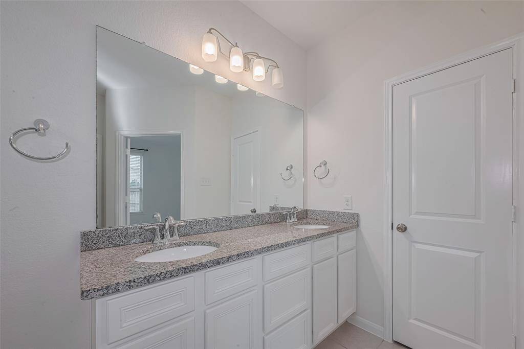 The primary bathroom measures 10'10" x 8'11" and features double sinks set in a granite countertop, offering both style and functionality. Raised cabinets provide ample storage, while a vanity light with frosted glass shades adds a soft, elegant glow to the space. This en-suite bath complements the primary suite with a clean, modern design.