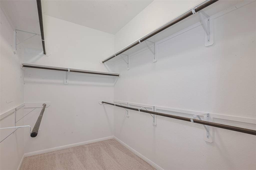 7’x10’2” walk-in closet with built-in shelving, hanging racks, and carpet.