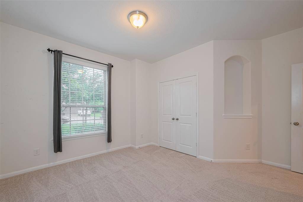This spacious 13'8" x 12'10" secondary bedroom features a double-door reach-in closet with built-in shelving and hanging racks, offering excellent storage and organization. The room is finished with new carpet (2025) and a dome ceiling light for a cozy, well-lit atmosphere. A large window with 2" faux wood blinds brings in natural light, while an art niche adds a stylish architectural detail.
