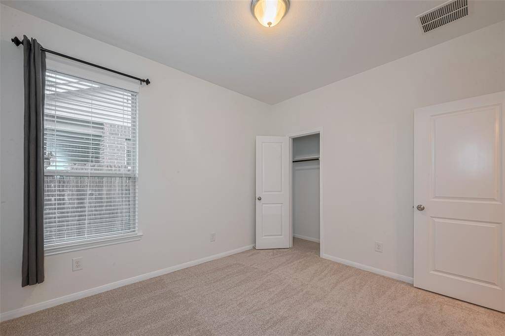 This 9'11" x 11'1" secondary bedroom offers a cozy and functional layout. It features new carpet (2025), a large window with 2" faux wood blinds for natural light and privacy, and a dome ceiling light for ambient illumination. The reach-in closet includes built-in shelving and hanging racks, maximizing storage efficiency.