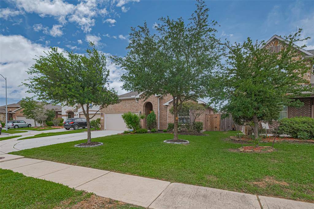 The home features a classic brick exterior, offering timeless curb appeal and low-maintenance durability. A double-wide driveway provides ample parking space and easy access to the garage. The front yard is enhanced by professional landscaping, beautifully accented with a stone border that adds definition and charm to the greenery.