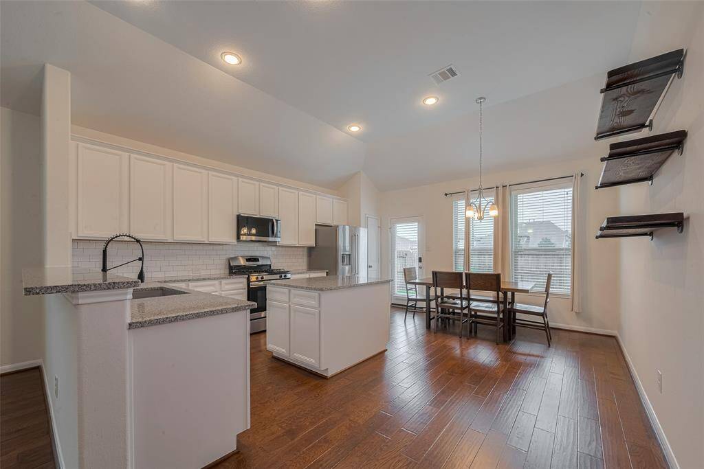 This expansive 16'6" x 17'8" kitchen combines style and functionality with granite countertops and raised cabinets that offer ample storage. A reach-in pantry with built-in shelving provides organized space for dry goods and kitchen essentials. The breakfast bar adds a casual dining option.