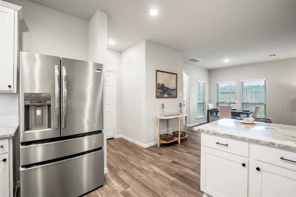 This sleek stainless steel fridge (yep—it stays!) anchors the kitchen with style and function. Just behind it, you'll find a dedicated pantry with ample shelf space to keep essentials organized and out of sight. From here, you also get a great view of the breakfast nook and back patio access—proof this layout is as efficient as it is inviting.