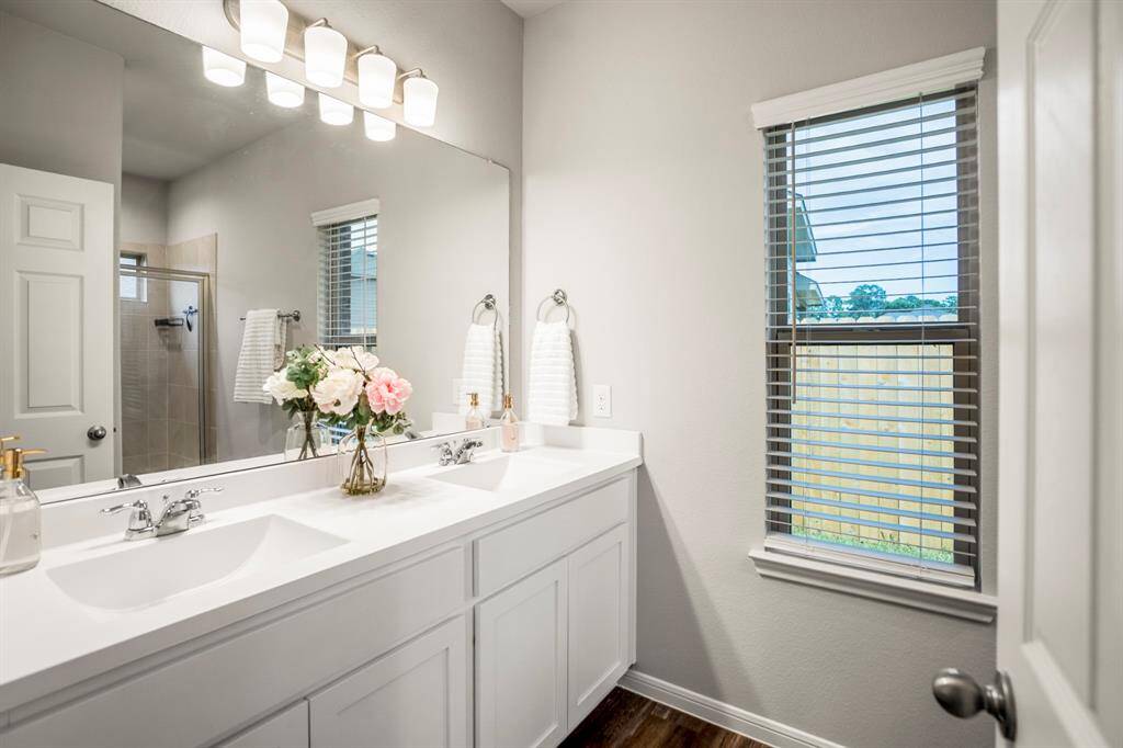 The en suite primary bath is bright, clean, and thoughtfully designed with a double vanity—no more elbow-bumping during busy mornings. A large framed mirror and soft lighting give the space an open feel, and the window brings in natural light while keeping privacy intact. Just out of frame? A walk-in shower with dual Kohler shower heads for a more spa-like experience.