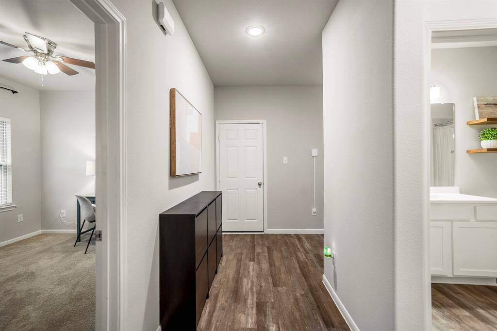 From this hallway, you can see into one of the two secondary bedrooms—both of which include upgraded ceiling fans for added comfort. Just to the right, a smaller hallway leads to the guest bath and the second bedroom, keeping the layout private and functional. You won’t spot them in this photo, but smart smoke detectors with built-in carbon monoxide sensing are also installed in the home—one of several thoughtful upgrades throughout.