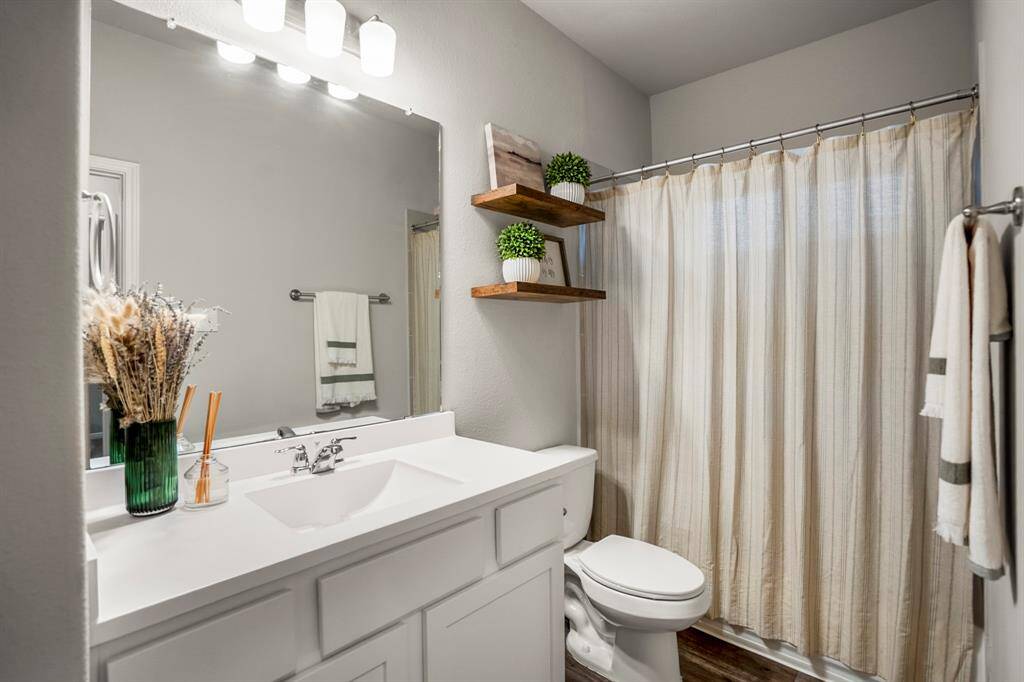 The full guest bath is simple, stylish, and ready to serve—whether it’s daily routines or weekend visitors. A clean white vanity with storage, open shelving for added charm, and a full tub/shower combo make the space feel both functional and welcoming. Bonus: all toilets throughout the home were upgraded with slow-close seats for a quieter touch of convenience.